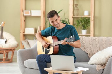 Yakışıklı adam evde gitar çalıyor.