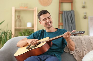 Yakışıklı adam evde gitar çalıyor.