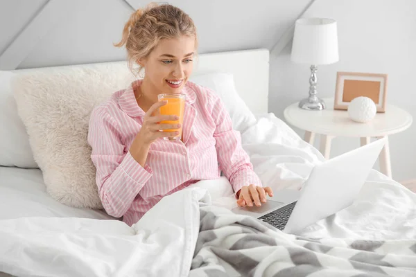Morning of beautiful young woman with laptop drinking juice in bed — Stock Photo, Image