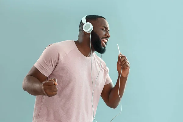 African-American man listening to music and singing on color background — Stock Photo, Image