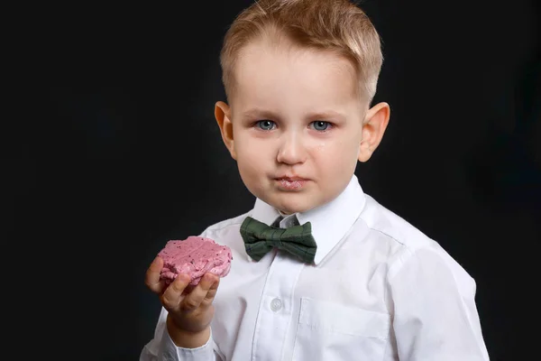 Портрет плачущего мальчика со сладким безе на темном фоне — стоковое фото