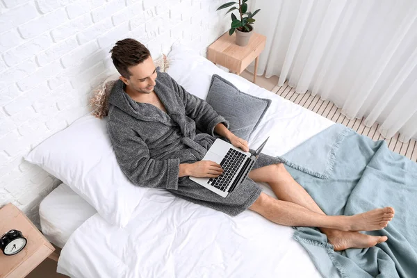 Handsome man in bathrobe using laptop on bed — Stock Photo, Image