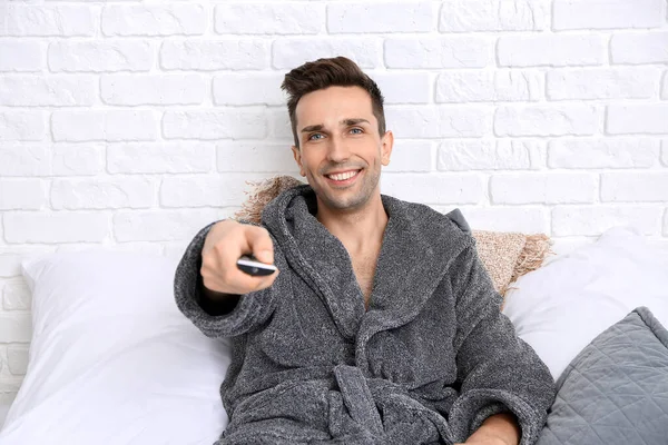 Handsome man in bathrobe watching TV on bed — Stock Photo, Image