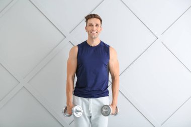 Işık arka plan üzerinde dumbbells ile sportif genç adam