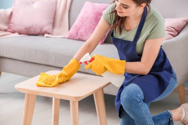 Kadın hademe odada masayı temizliyor.