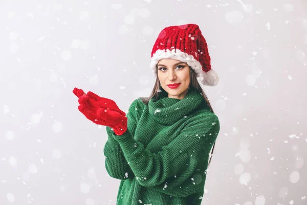 Beautiful young woman in Santa hat and falling snow on light background — Stock Photo, Image