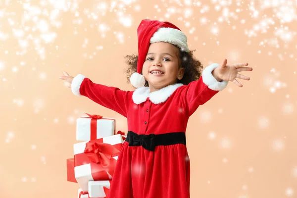 Pequena menina afro-americana em traje de Papai Noel e com presentes em fundo de cor com neve — Fotografia de Stock