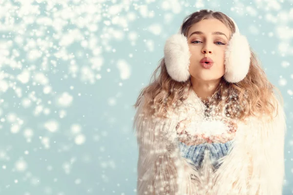 Šťastná mladá žena v zimě oblečení foukání sníh na barevném pozadí — Stock fotografie