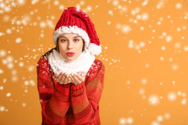 Young woman in winter clothes blowing snow on color background — Stock Photo, Image