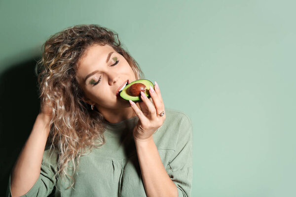 Fashionable young woman with avocado on color background