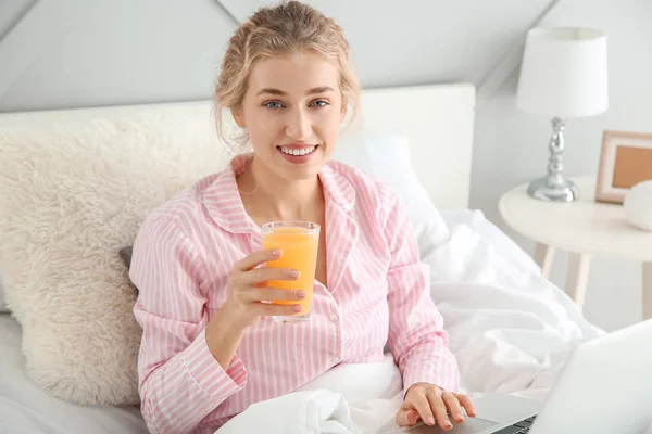 Morning of beautiful young woman with laptop drinking juice in bed — Stock Photo, Image