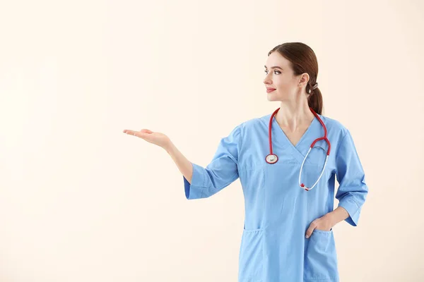 Portrait of female doctor showing something on light background — Stock Photo, Image