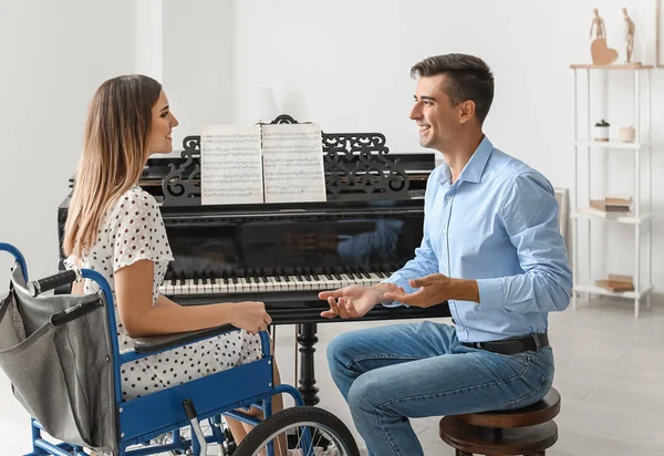 휠체어를 타고 있는 젊은 여자에게 피아노치는 법을 가르치는 남자 — 스톡 사진