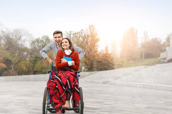 Handicapped young woman in wheelchair and her husband outdoors — Stock Photo, Image