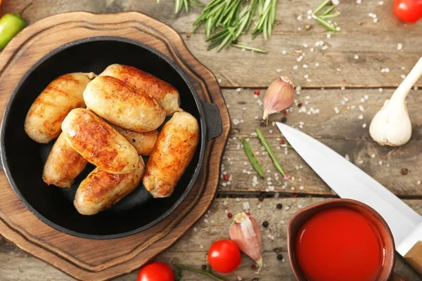 Frying pan with tasty grilled sausages on wooden table — Stock Photo, Image