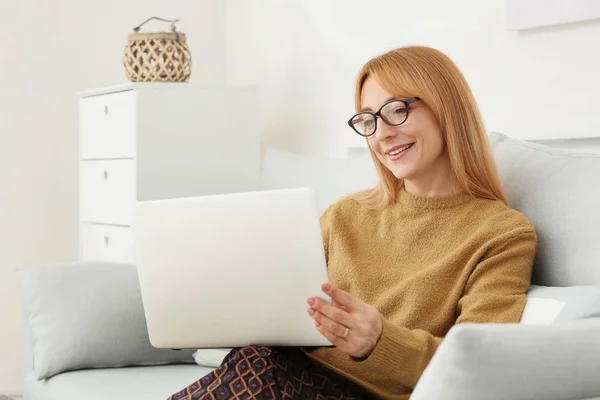 Bella donna matura con computer portatile seduto sul divano a casa — Foto Stock