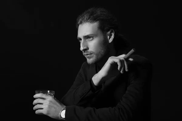 Černobílý portrét pohledného podnikatele s alkoholem a doutníkem na tmavém pozadí — Stock fotografie