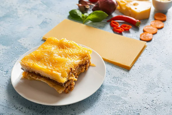 Placa con sabrosa lasaña al horno y los ingredientes en el fondo de color —  Fotos de Stock