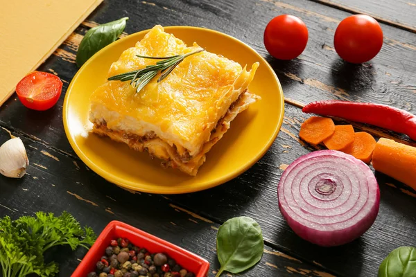 Assiette avec lasagnes cuites au four savoureuses et ingrédients sur fond de bois foncé — Photo
