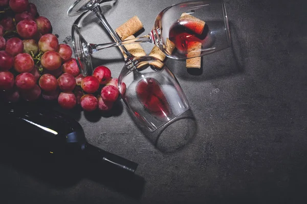 Бутылка вина с виноградом, бокалами и пробками на темном фоне — стоковое фото