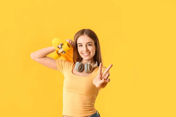 Stylish hipster girl with skateboard showing victory gesture on color background — Stock Photo, Image