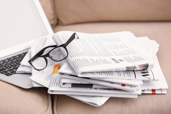 Stack of newspapers and laptop on sofa