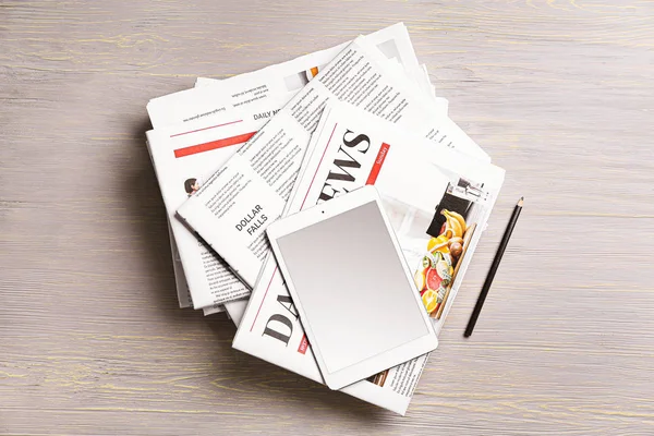 Stack of newspapers and tablet computer on wooden background — Stock Photo, Image