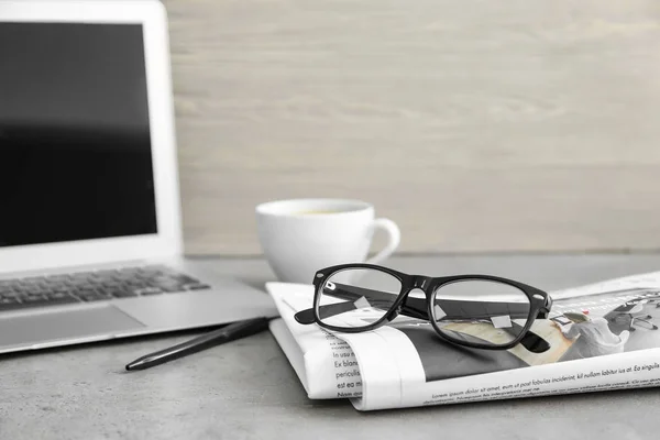 Газета, ноутбук и очки на столе — стоковое фото