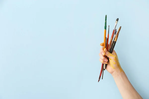 Hand des Künstlers mit Pinseln auf farbigem Hintergrund — Stockfoto