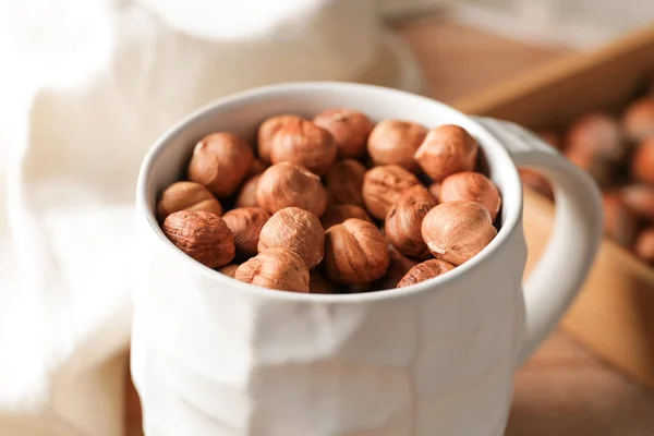 Mug with tasty hazelnuts on table, closeup — Stock Photo, Image
