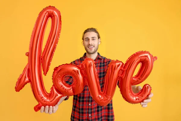 Handsome man with air balloon in shape of word LOVE on color background. Valentine's Day celebration — Stock Photo, Image