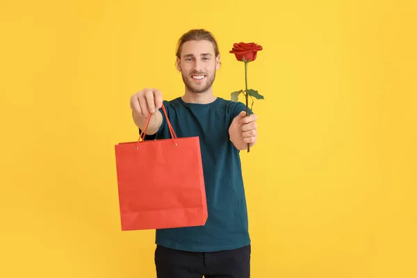 Handsome man with flower and gift on color background. Valentine's Day celebration — Stock Photo, Image