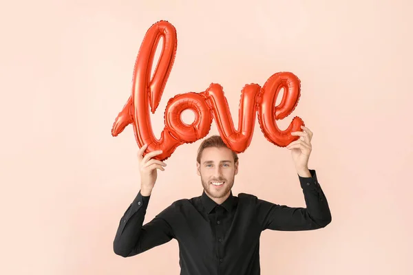 Hombre guapo con globo aerostático en forma de palabra AMOR sobre fondo de color. Celebración de San Valentín —  Fotos de Stock