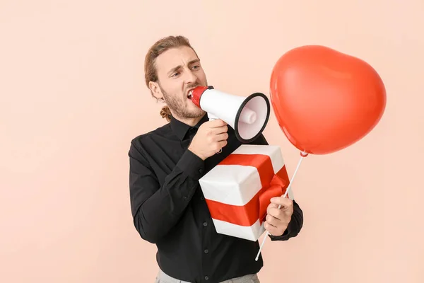 Screaming man with megaphone, gift and air balloon on color background. Valentine's Day celebration — Stock Photo, Image