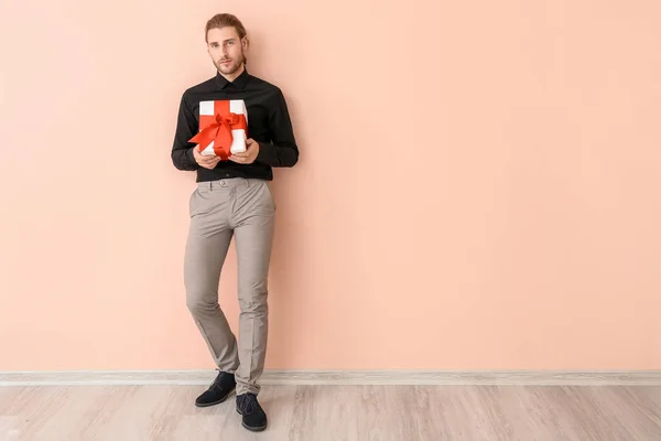 Hombre guapo con regalo cerca de la pared de color. Celebración de San Valentín —  Fotos de Stock