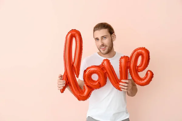 Hombre guapo con globo aerostático en forma de palabra AMOR sobre fondo de color. Celebración de San Valentín —  Fotos de Stock