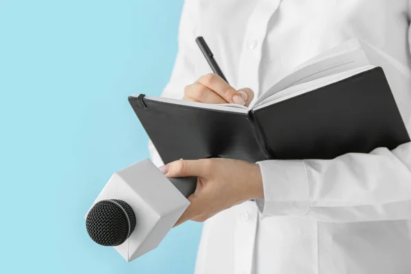 Journalist with microphone writing in notebook against color background — Stock Photo, Image