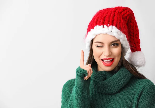 Mulher bonita no chapéu de Santa e com dedo indicador levantado no fundo claro — Fotografia de Stock