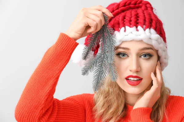 Mulher bonita em chapéu de Santa e com galho de árvore de Natal no fundo claro — Fotografia de Stock