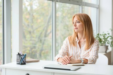 Güzel, olgun bir kadın iş yerinde oturuyor.