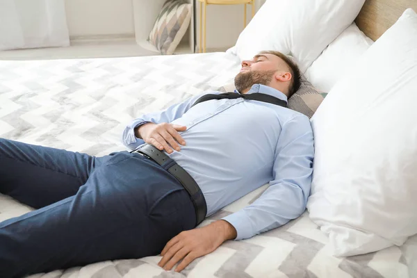 Tired businessman in formal clothes sleeping on bed