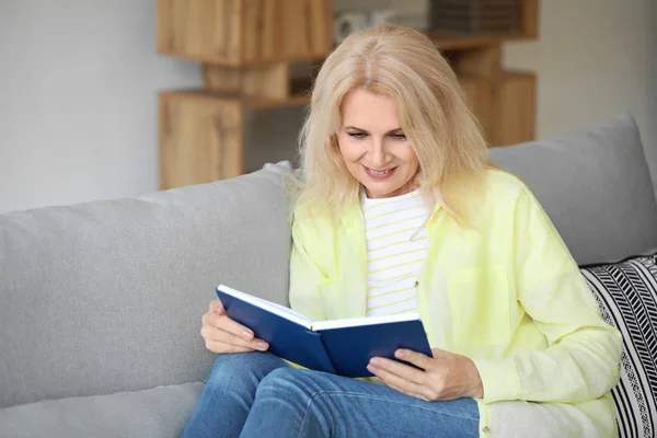 Evde kitap okuyan güzel olgun bir kadın. — Stok fotoğraf