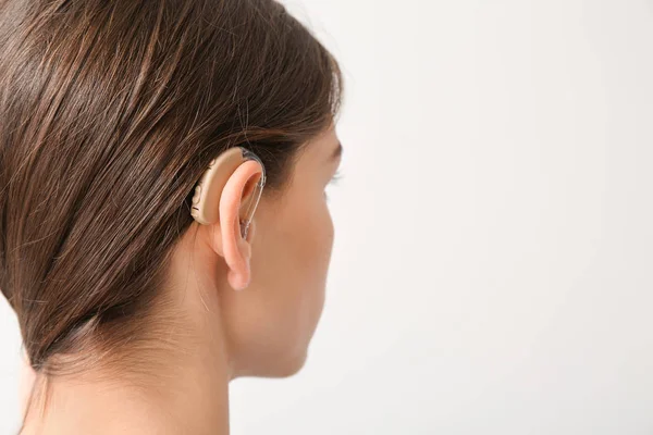 Νεαρή γυναίκα με ακουστικό βαρηκοΐας σε ελαφρύ φόντο — Φωτογραφία Αρχείου