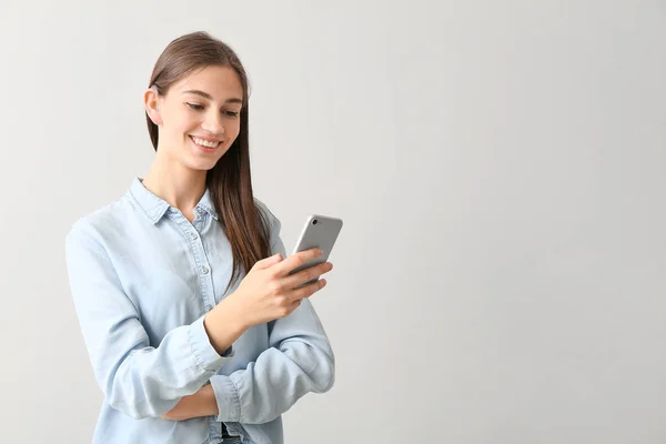 Jonge vrouw met gehoorapparaat en mobiele telefoon op lichte achtergrond — Stockfoto
