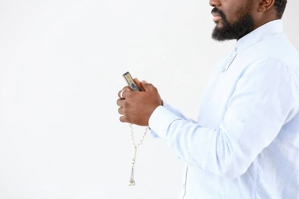 African-American Muslim man with Koran and beads on light background — Stock Photo, Image