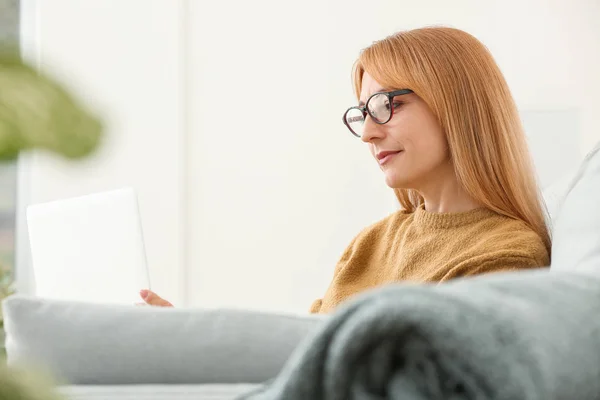 Bella donna matura con computer portatile seduto sul divano a casa — Foto Stock