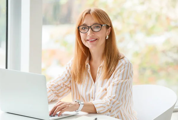 Beautiful mature woman sitting at workplace in office — Stock Photo, Image