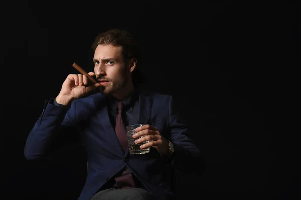 Porträt eines gutaussehenden Geschäftsmannes mit Alkohol und Zigarre auf dunklem Hintergrund — Stockfoto
