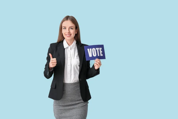 Junge Geschäftsfrau hält Papier mit Text-Abstimmung und zeigt Daumen nach oben auf farbigem Hintergrund — Stockfoto