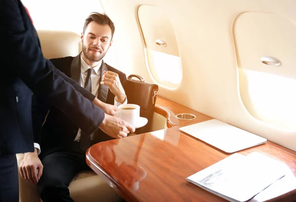 Air hostess bringing coffee for businessman on board the modern private airplane